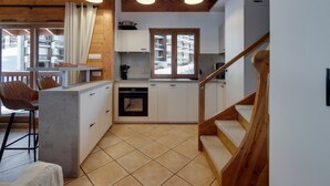 A modern kitchen with wooden beams, a dining area with a chair, and a view of a snowy landscape through a window. - 9-person apartment with parking in Tignes Val Claret (Tignes)