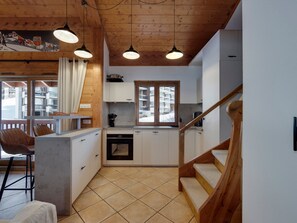Uma cozinha moderna com vigas de madeira, um espaço de refeições com uma cadeira e vista para uma paisagem nevada através de uma janela.