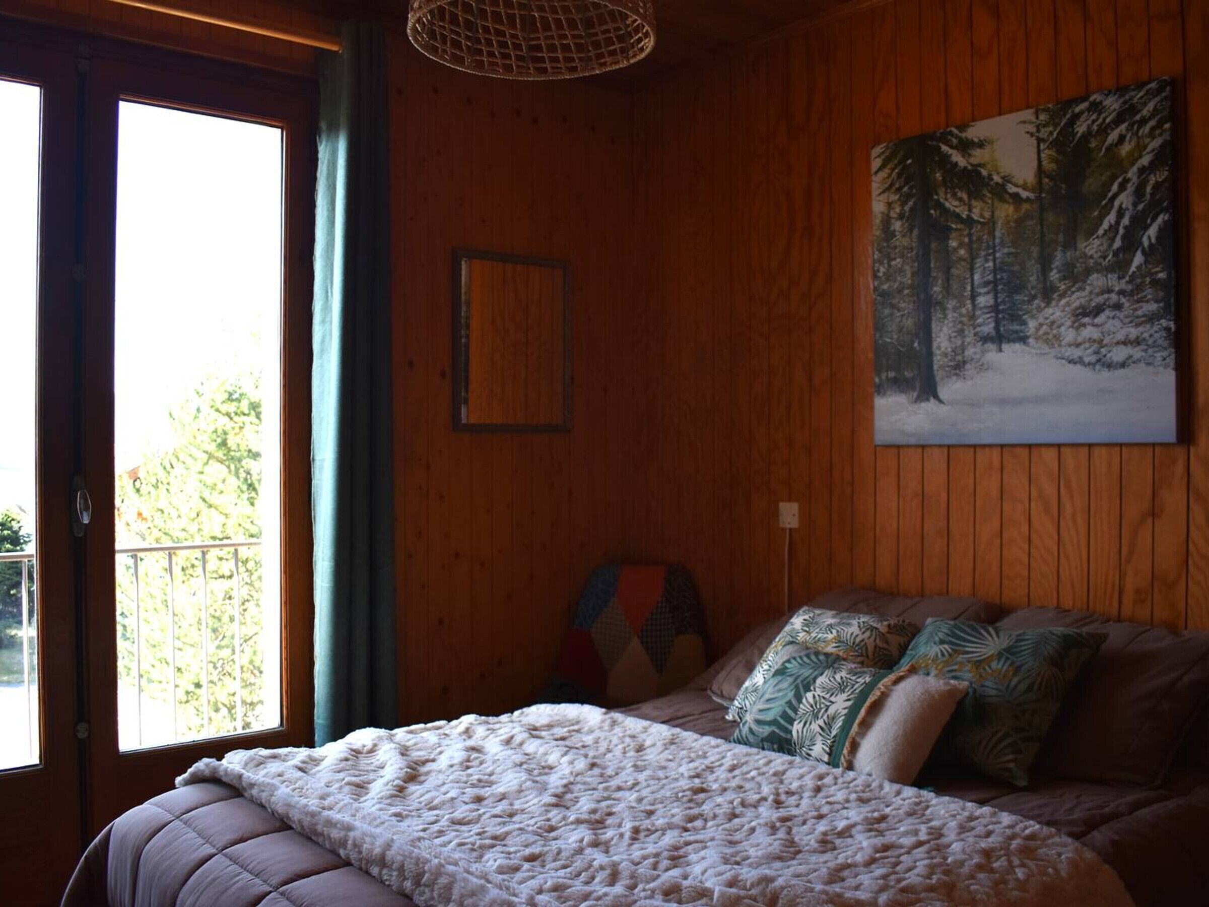 Et hyggeligt soveværelse med en stor seng, et billede af en sneklædt skov og en balkon med udsigt til træer.