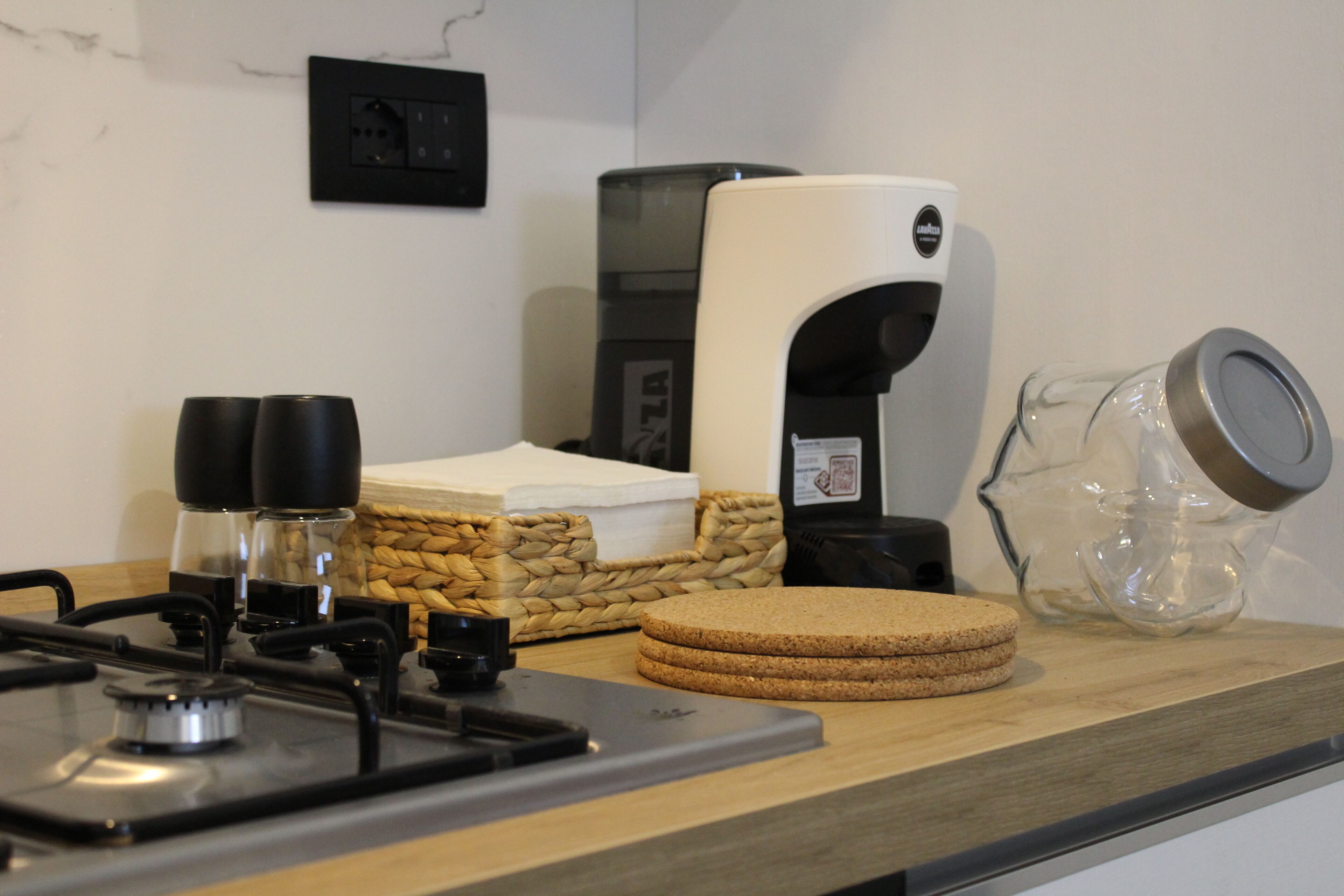Una encimera de cocina con una cafetera, un tarro de vidrio y una pila de pan.