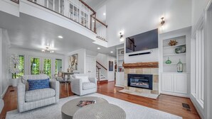 A spacious living room with a fireplace, a staircase, and a balcony. - Black Bear Ridge | Games, Hot Tub, Deck w/ Views (Mentone)