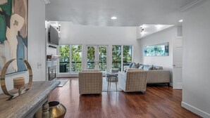 A spacious living room with a large window, a sofa, a coffee table, and a wooden floor. - Black Bear Ridge | Games, Hot Tub, Deck w/ Views (Mentone)