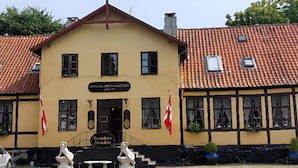 Un bâtiment jaune avec une enseigne indiquant « Traneker Slottkro » et deux drapeaux.