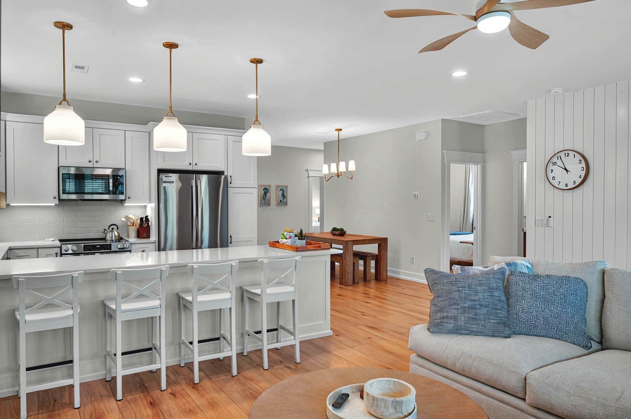 A modern kitchen with white bar stools, a dining table, and a ceiling fan.