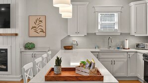 Een moderne keuken met witte kasten, een centraal eiland en een eethoek met witte stoelen.