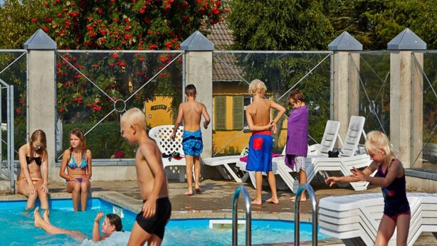 Un espace piscine doté d’une terrasse en béton, de chaises longues et d’une clôture.