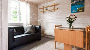 A modern living room with a black leather sofa, wooden dining table, and a painting of a coastal scene. - 6 Person Holiday Park Home in Asperup (Middelfart)