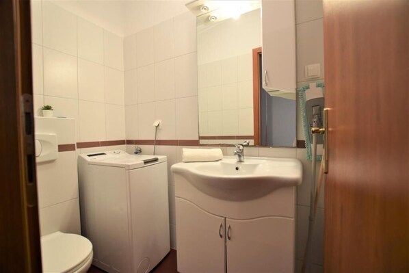 Une petite salle de bain comprenant des toilettes, un lave-linge, un lavabo et un miroir.