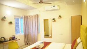 Une chambre d’hôtel comprenant un lit, un bureau, une chaise, une fenêtre avec des rideaux, un miroir et un ventilateur de plafond.