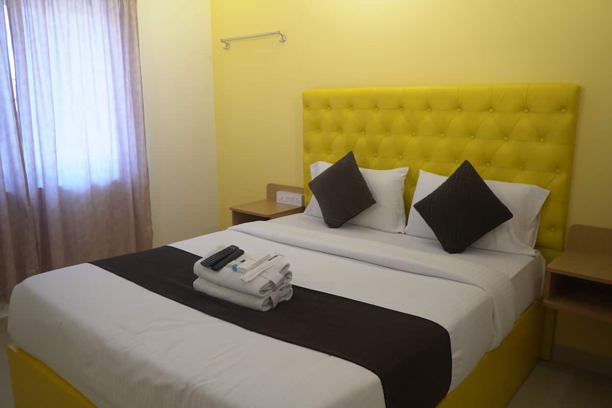 Habitación de hotel con cabecera amarilla, ropa de cama blanca y cama bien hecha con toallas y un control remoto.