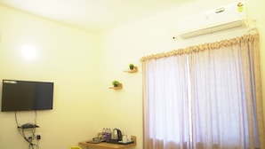 Une chambre dotée d’un téléviseur à écran plat fixé au mur, d’un bureau avec une chaise, d’une petite table avec une bouilloire et des tasses, et d’une grande fenêtre avec des rideaux.
