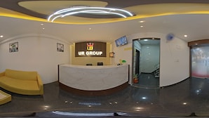 Un espace d’accueil moderne avec un comptoir en marbre, un canapé jaune et un bureau de réception où figure le logo « UR GROUP ».