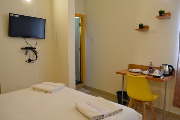 A hotel room with a bed, a desk with a chair, a television mounted on the wall, and a small shelf with plants. - UR Stay Inn (Bengaluru)