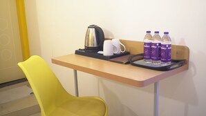 Une chambre d’hôtel avec un bureau en bois, une chaise jaune, une bouilloire, deux tasses blanches et trois bouteilles d’eau à la Bailey’s.