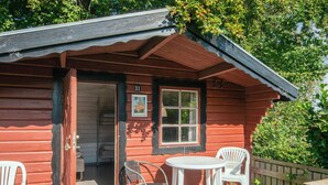 Een houten chalet met een veranda, twee witte stoelen en een kleine tafel.