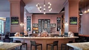 A bar area with a central island, bar stools, and a television screen. - Across Raleigh Convention Center + Dining & Pool (Raleigh)