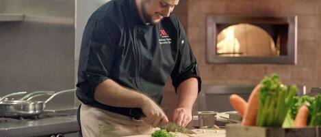 A chef in a kitchen with a brick wall and a wood-fired oven.
