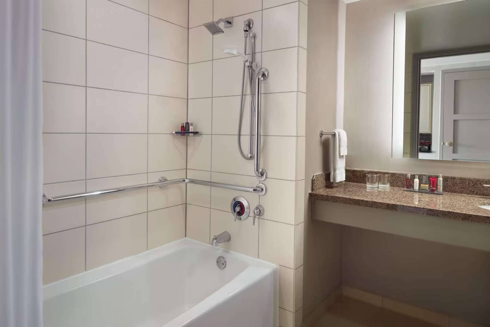 Un bany modern amb banyera, dutxa amb plat de roba i un lavabo amb mirall.