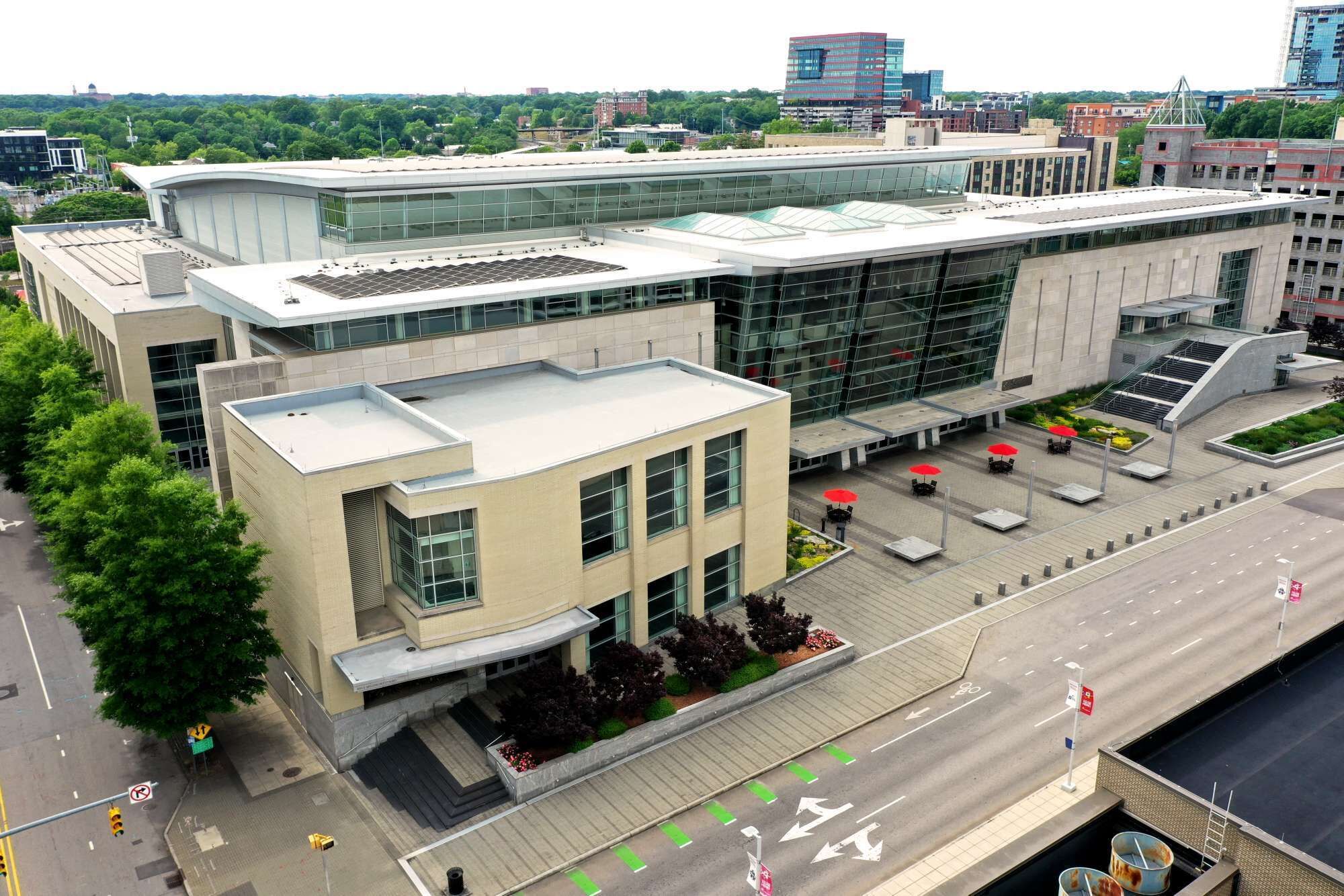 A modern building with a glass facade, a flat roof, and a parking area with umbrellas.