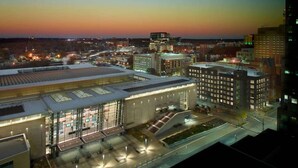 A modern building with a large glass facade, surrounded by other high-rise buildings. - Near Red Hat Amphitheater + Dining. Pool. Gym. (Raleigh)