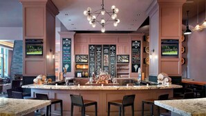 A bar area with a central island, bar stools, and a television screen. - Near Red Hat Amphitheater + Dining. Pool. Gym. (Raleigh)