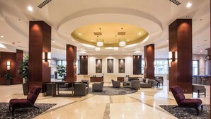 A spacious lobby with a central seating area, a reception desk, and a large, curved ceiling with pendant lighting. - Near Red Hat Amphitheater + Dining. Pool. Gym. (Raleigh)