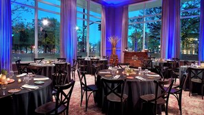 A restaurant with round tables and chairs, large windows, and a view of the outdoors. - Near Red Hat Amphitheater + Dining. Pool. Gym. (Raleigh)