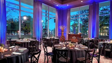 A restaurant with round tables and chairs, large windows, and a view of the outdoors.