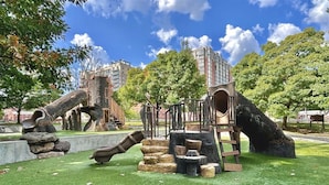 Un parque infantil con toboganes y estructuras para escalar, rodeado de árboles y un edificio al fondo.