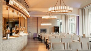 Un interior de restaurante moderno con una larga barra, varias lámparas colgantes y filas de mesas y sillas.