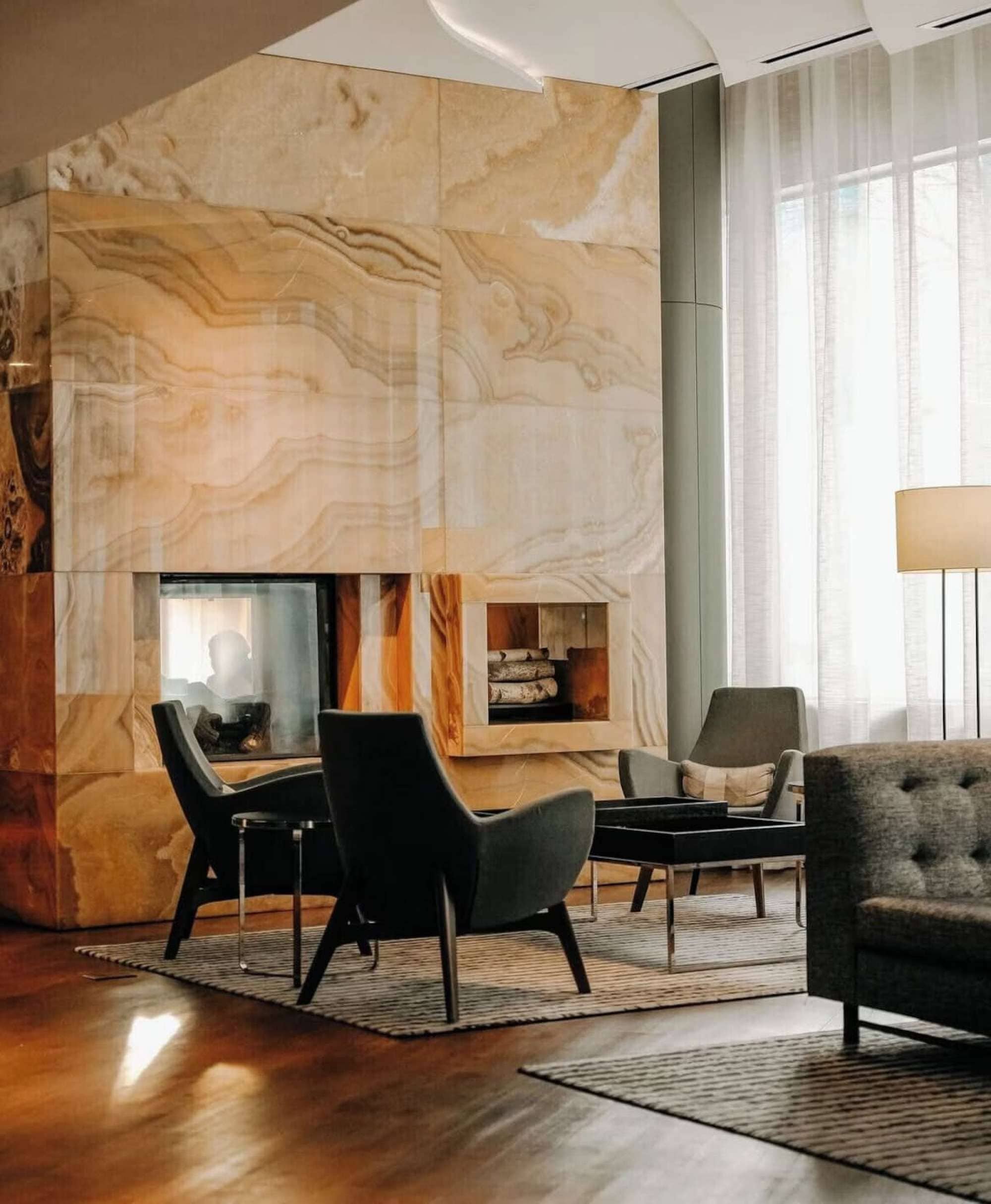 Una sala de estar moderna con una pared de mármol, una chimenea y un área de estar con un sofá y sillones.
