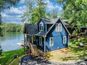 A blue house with a dock, a wooden staircase, and a grassy yard. - Lakefront Home with Dock, Hot Tub & Views (Robbinsville)