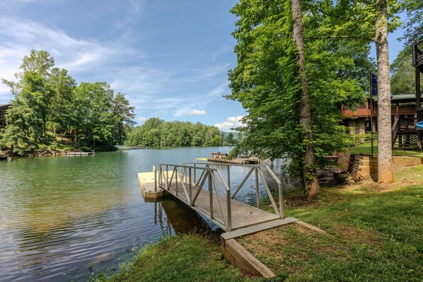 A wooden dock extending into a calm lake, surrounded by lush greenery and a clear sky. - Lakefront Home with Dock, Hot Tub & Views (Robbinsville)