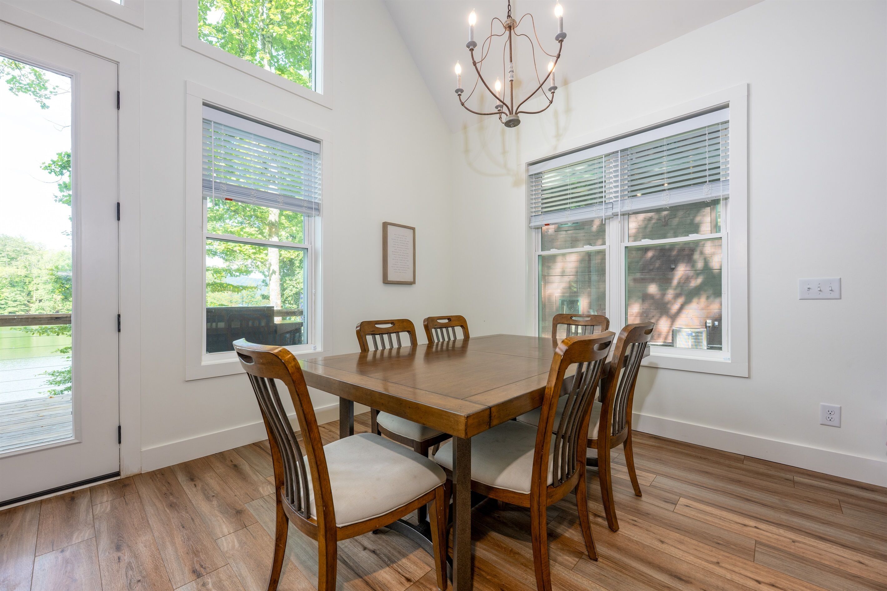 Une salle à manger avec une table et des chaises en bois, de grandes fenêtres et un lustre.