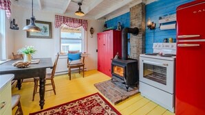Une cuisine avec un réfrigérateur rouge, une cuisinière blanche et un poêle à bois noir. On y trouve une table à manger avec des chaises et un tapis rouge sur le sol.