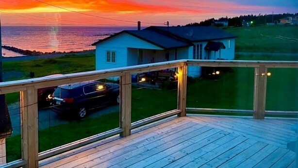 Une terrasse en bois offrant une vue sur une maison et l’océan au coucher du soleil.