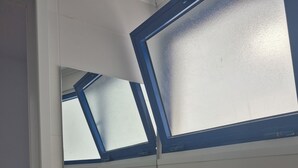 A bathroom with a white sink, a mirror, and a window with blue trim.