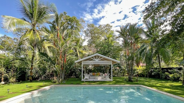 Una piscina con sedie a sdraio, un gazebo e vegetazione tropicale.