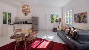 Een ruime woonkamer met een bank, eettafel, stoelen en een keuken op de achtergrond.