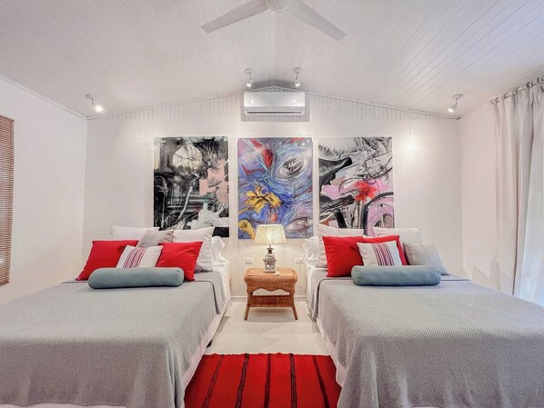 Un dormitorio moderno con dos camas, una mesita de noche central y tres grandes cuadros abstractos en la pared.