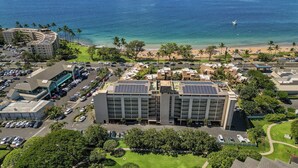 A hotel with a parking lot, a beach view, and solar panels on the roof. - #510-Ocean and Sunset Views! Steps from It All! (Kihei)