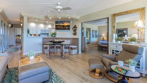 A spacious living area with a dining table, seating, a ceiling fan, and a kitchen in the background. - #510-Ocean and Sunset Views! Steps from It All! (Kihei)