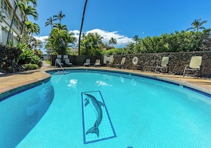 A swimming pool with a dolphin tile design, surrounded by lounge chairs and palm trees.