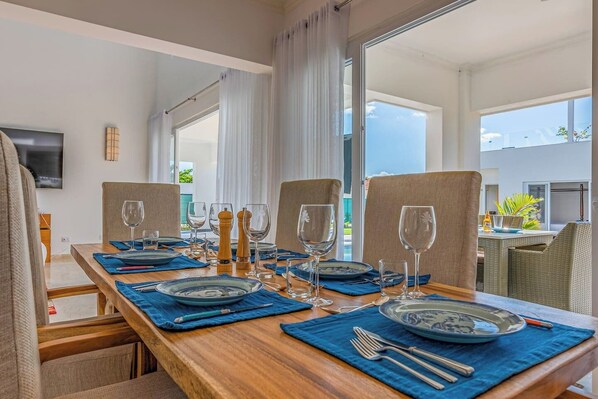 Comedor con una mesa de madera preparada para cuatro, individuales azules y cristalería transparente.