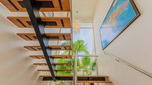 A modern staircase with wooden steps and metal supports, leading to a balcony with a view of palm trees and a map on the wall.