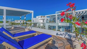 A rooftop terrace with blue lounge chairs, a pergola, and a view of the sea.