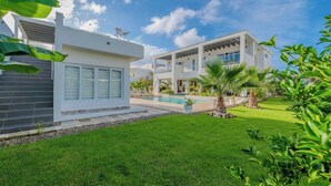 A modern two-story house with a swimming pool, a well-maintained lawn, and tropical plants.