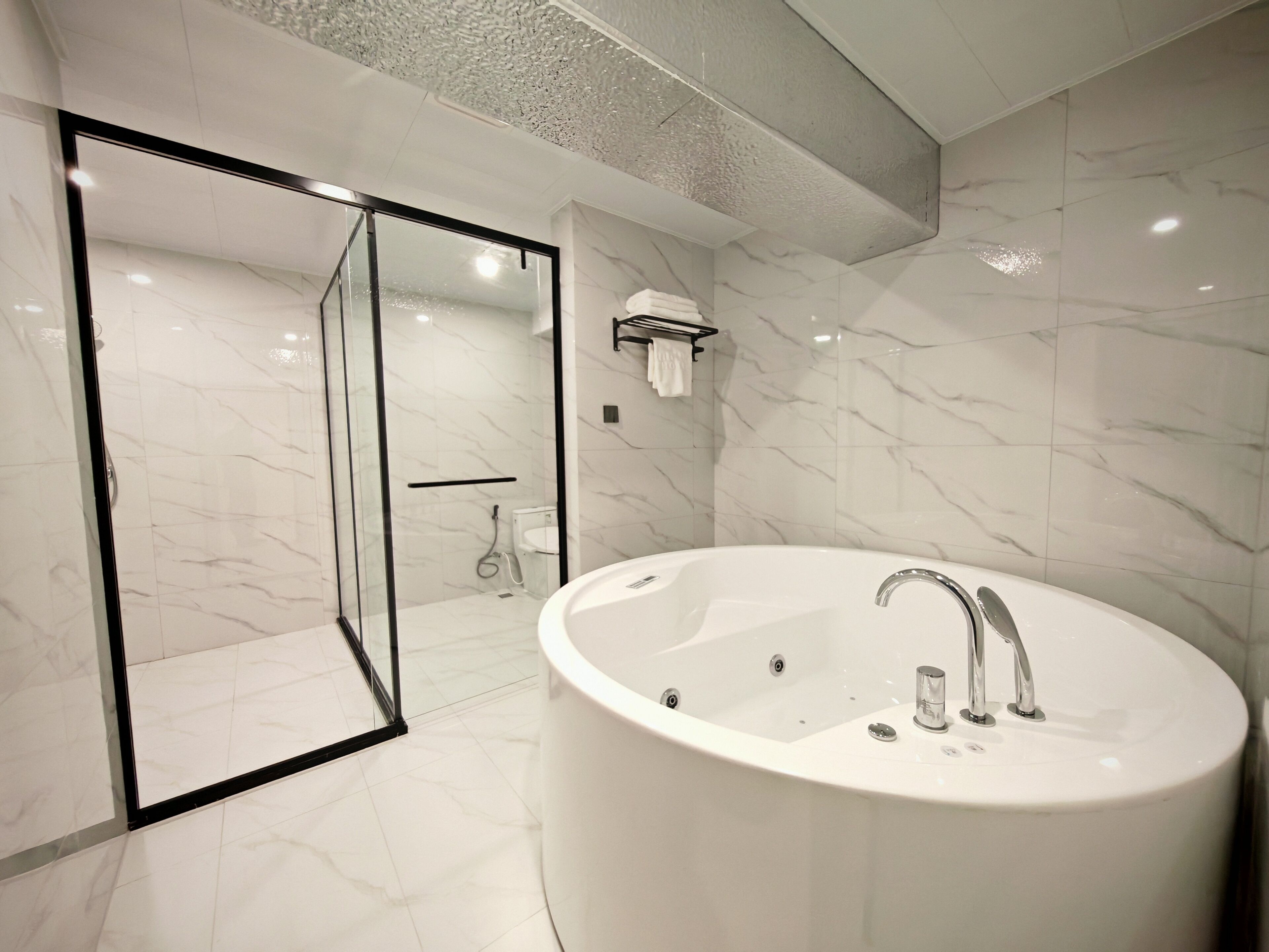 Un baño moderno con una bañera grande, cabina de ducha de vidrio y suelo de mármol.