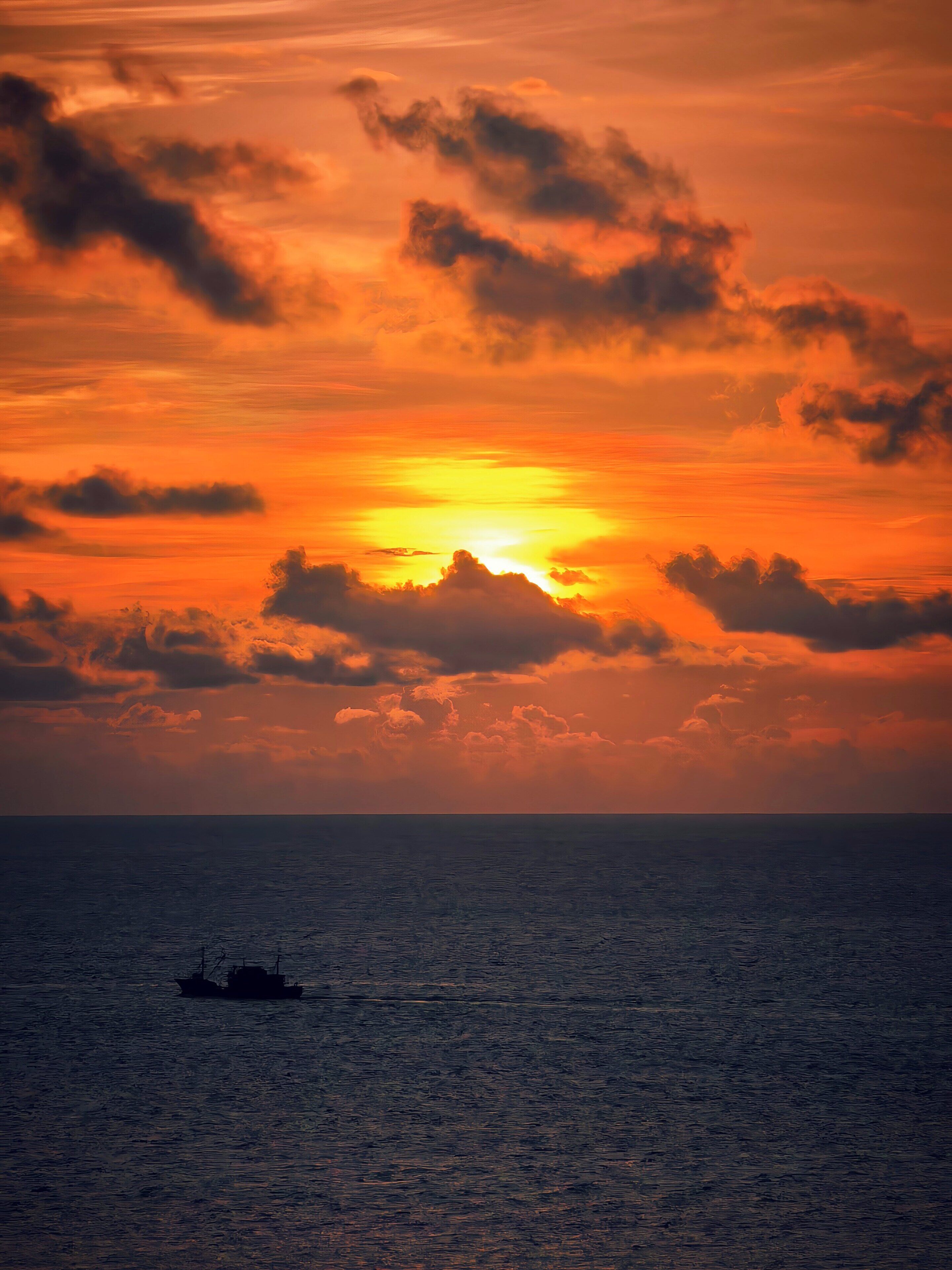 A sunset over the ocean with a boat in the distance.