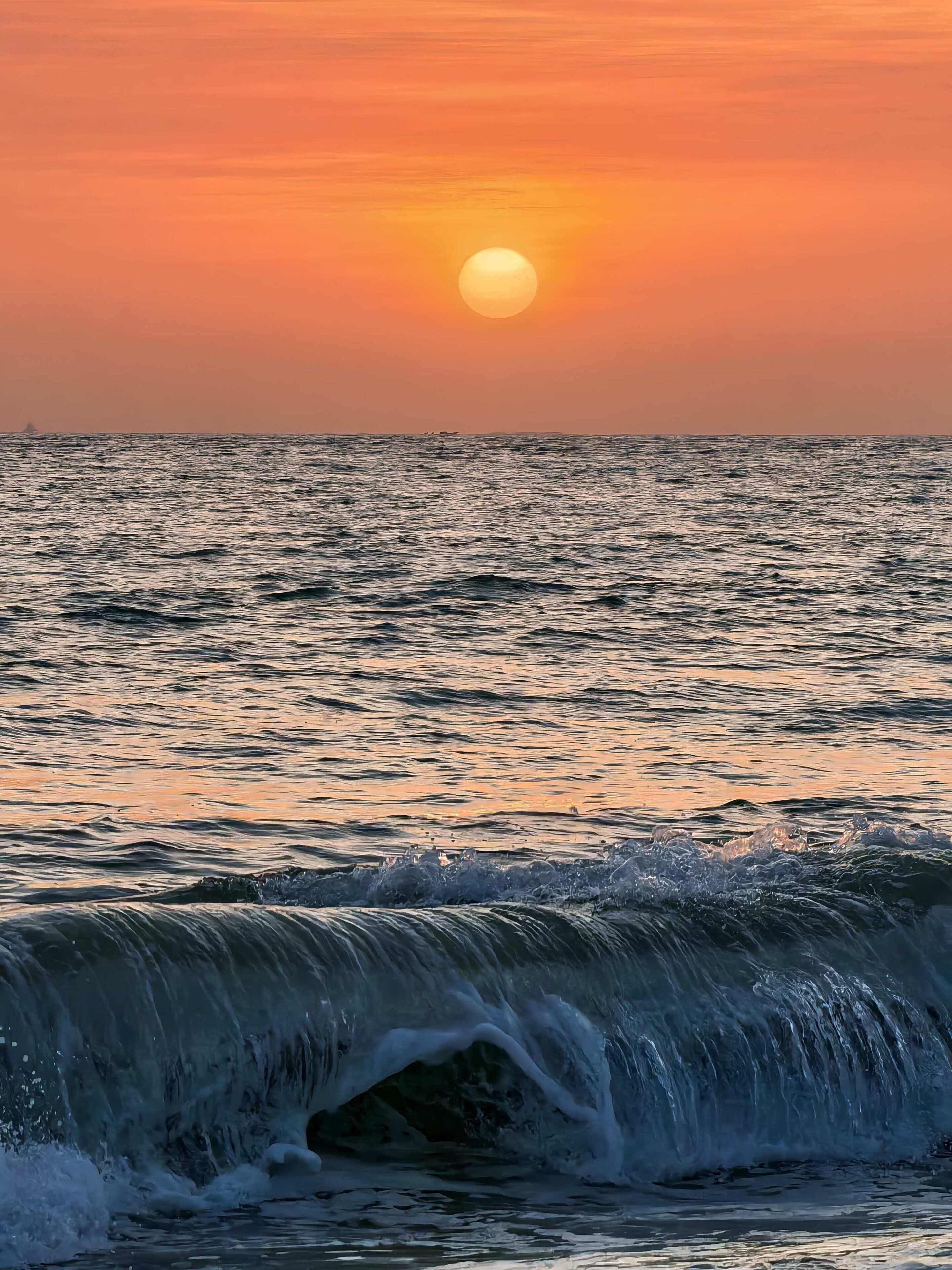 A sunset over the ocean with waves crashing onto the shore.